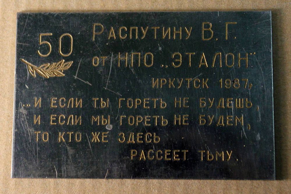 Металлическая табличка с надписью «Распутину В. Г. от НПО «Эталон». Иркутск. 1987». Также надпись «И если ты гореть не будешь, и если мы гореть не будем, то кто же здесь рассеет тьму». Размер 4,8 х 7 см.